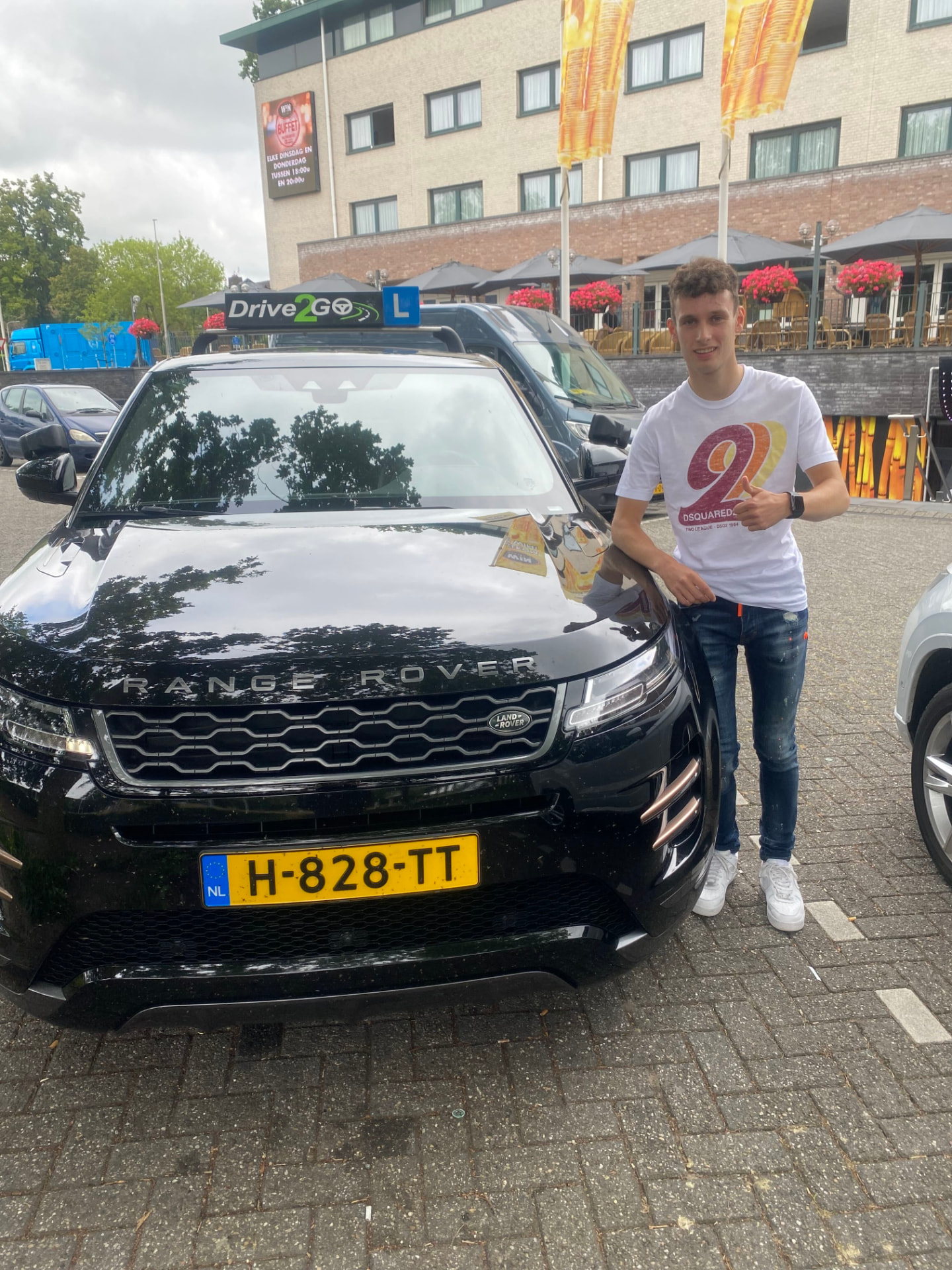 Geslaagde leerling met duim bij de lesauto