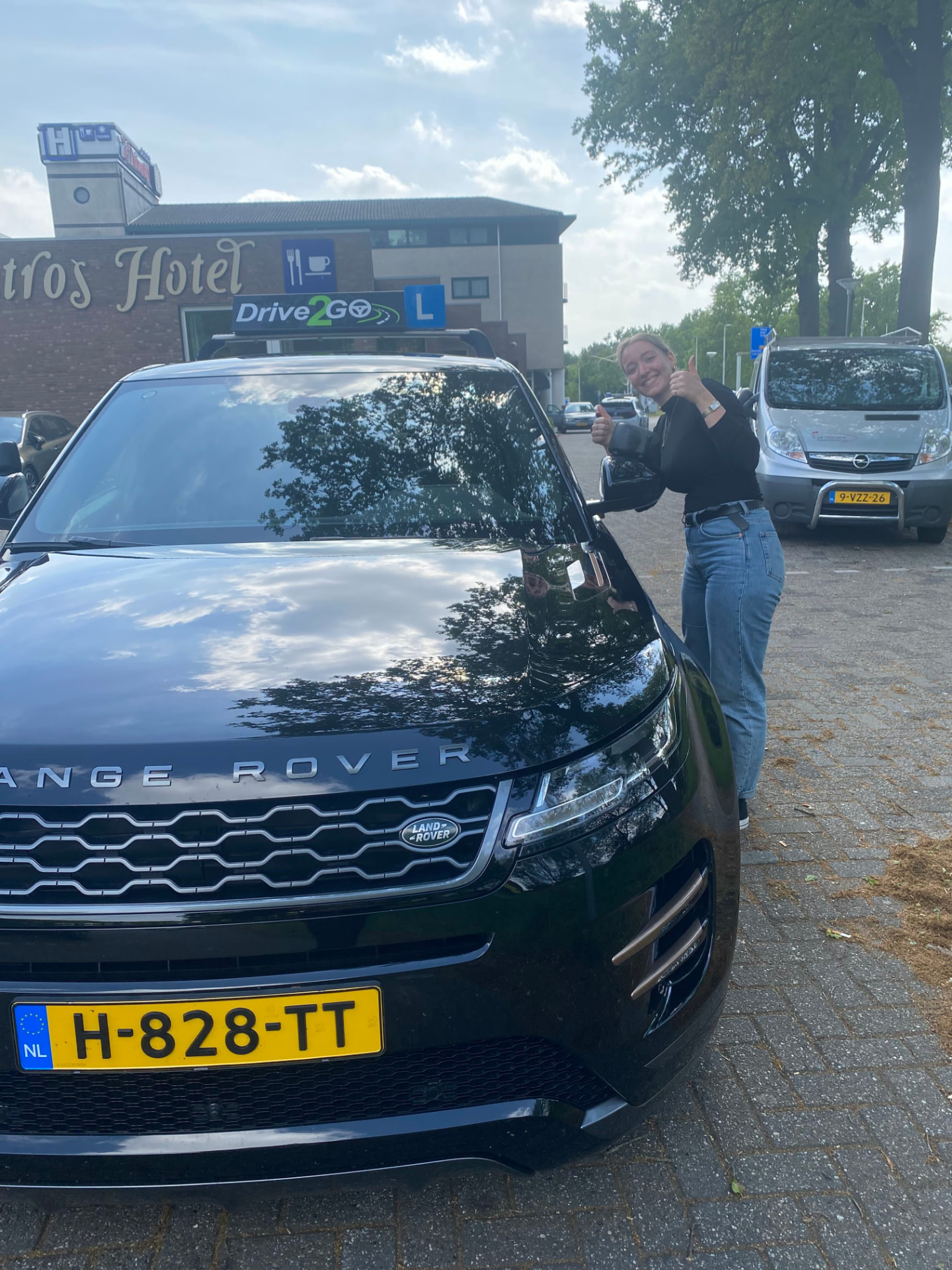 Geslaagde leerling met duim naast de lesauto