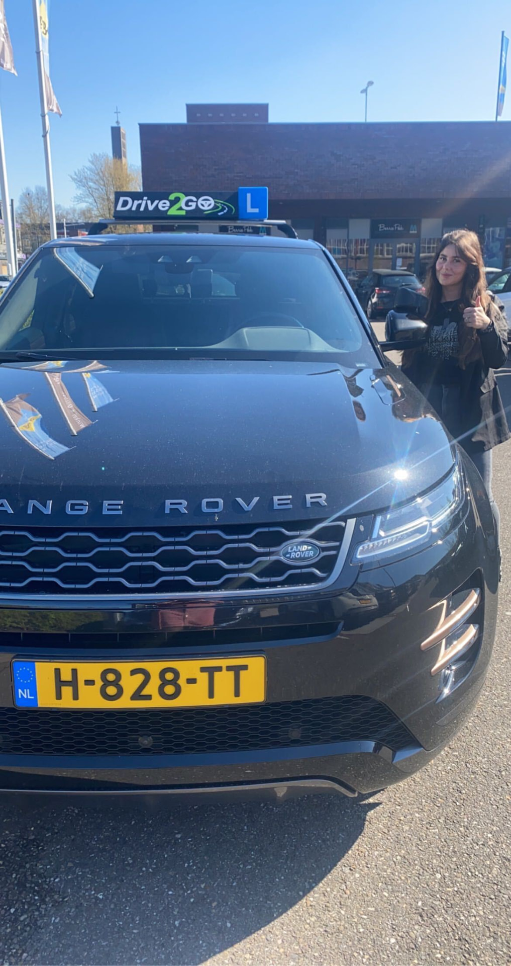 Geslaagde leerling in de zon bij de lesauto